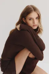 Top de manga larga color marrón oscuro, confeccionado en tejido de punto acanalado. Presenta un cuello camisero que se abre en un escote pronunciado en V.