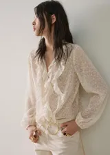 Blusa de tejido fluido color crudo, con escote en V, mangas largas y volantes decorativos en el frente y cuello.