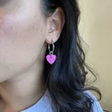 Par de aros plateados tipo argolla con dije de corazón rosa chicle.