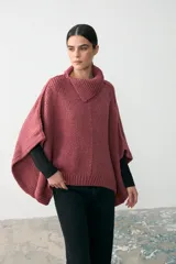 Capita de tejido de punto grueso en color rosa, con cuello alto y diseño holgado tipo poncho con aberturas laterales para los brazos.