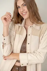 Camisa de cuero ovino color beige claro, estilo western, con canesú en los hombros en gamuza de tono similar. Presenta costuras contrastantes y cierre frontal con broches. Posee bolsillos laterales.