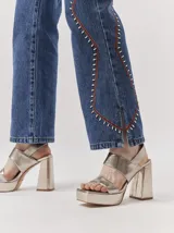 Sandalias de plataforma con taco cuadrado alto, confeccionadas en cuero metalizado color dorado. Presentan un diseño de tiras anchas cruzadas en el empeine y cierre con pulsera al tobillo.