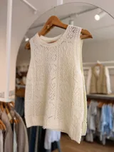 Musculosa tejida de color natural, con diseño calado de motivos geométricos y florales, escote redondo y silueta sin mangas.