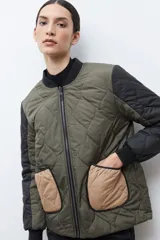 Campera bomber reversible con diseño capitoneado, cuerpo en color verde oliva y mangas negras. Presenta cierre frontal, cuello, puños y ruedo acanalados, y un bolsillo de parche en color beige.