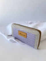 Billetera grande de cuero con cierre metálico perimetral. Presenta un diseño rectangular con textura tipo reptil, monedero interno y espacio para billetes extendidos.