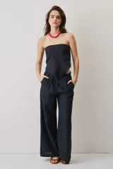 Pantalón de lino negro de corte holgado y pierna ancha, con bolsillos laterales y cierre frontal.