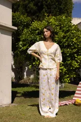 Conjunto de dos piezas compuesto por una camisa de manga corta abullonada con escote en V y cierre frontal de botones, y un pantalón de corte recto y holgado. Ambas prendas presentan un estampado floral en tonos amarillos sobre fondo blanco.