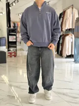 Buzo gris oscuro de corte oversize con cuello alto y cierre frontal parcial. Cuenta con mangas largas y puños elásticos, además de un pequeño bordado con texto en el pecho.