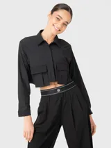 Blusa corta negra de manga larga con cuello camisero y dos bolsillos frontales con fuelle. Se puede usar abierta o cerrada. Combina con el pantalón Domi.
