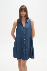 Vestido corto de denim sin mangas, con cuello camisero, cierre frontal con botones y diseño de falda con volados.