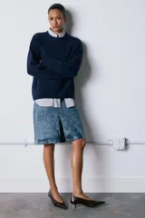 Falda midi de tiro medio confeccionada en denim con efecto lavado. Presenta cintura con trabillas, cierre frontal con cremallera, botón y gancho metálico, y una abertura en el bajo.
