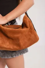 Bolso tipo hobo de gamuza color naranja quemado, con correa ancha de tela color bordó.