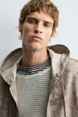 Cazadora negra de algodón con efecto lavado, corte relajado y capucha ajustable. Presenta cierre frontal de cremallera, bolsillos frontales tipo canguro y elásticos en puños y bajo.