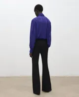 Blusa de manga larga en color azul eléctrico con diseño de rayas verticales sutiles. Presenta un cuello alto con detalle de lazo integrado y cierre frontal con botones ocultos. El tejido es semitransparente con acabado satinado.