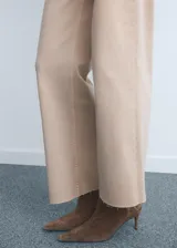 Jeans tiro alto estilo culotte de color beige claro, con diseño de pernera ancha, bajo deshilachado y cierre de cremallera y botón.