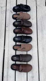 Mules de gamuza color tostado con diseño de tira ajustable con hebilla metálica y detalles de ojalillos decorativos. Posee plantilla ergonómica con logo grabado y suela plana de goma negra.