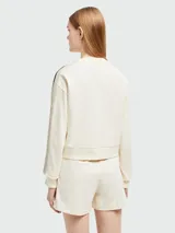 Sudadera color crema de corte holgado con cuello redondo y mangas largas. Presenta una banda lateral con diseño de tejido calado y logo de la marca en la manga izquierda.