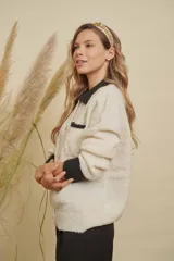 Saco de punto color crema con cuello, puños y detalle en el bolsillo en color negro. Presenta cierre frontal con botones dorados y diseño de corte recto.