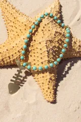 Collar de cuentas de cristal checo color turquesa y dorado, con dije de esqueleto de pez en bronce.