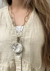 Collar de cadena de eslabones grandes en bronce, con un dije circular de bronce que contiene una pieza de guampa natural engarzada.