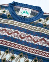 Buzo tejido de punto con diseño de patrones geométricos estilo nórdico en tonos azules, marrones, blancos y verdes. Presenta cuello redondo, puños y ruedo acanalados, con etiqueta de la marca Denali en el pecho.