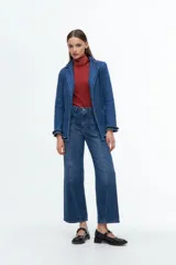 Blazer de denim azul con solapas y puños decorados con volados desflecados. Presenta un corte estructurado con bolsillos laterales y cierre frontal.