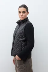 Chaleco capitoneado reversible con cuello alto, cierre frontal con botones a presión y bolsillos delanteros. Presenta un diseño bicolor en tonos verde oliva y beige con detalles en negro.