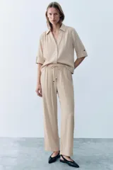 Camisa negra de textura arrugada, con cuello solapa, escote en V y cierre frontal de botones. Cuenta con mangas cortas terminadas en vuelta con trabilla y botón.