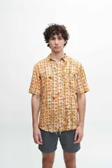 Camisa de manga corta con estampado de inspiración azteca en tonos naranja y amarillo. Confeccionada en algodón, presenta un cuello clásico y cierre frontal con botones.