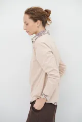 Remera de manga larga en color rosado, con cuello redondo y cierre frontal parcial con botones. Presenta un diseño de corte recto y estilo minimalista.