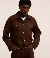 Campera trucker marrón, de corte overboxy y manga larga, confeccionada en sarga de algodón. Tiene cuello inglés, cierre abotonado, bolsillos con solapa y pespunte contrastante.