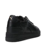 Championes urbanos Puma modelo Shuffle Downtown, de color negro con detalles en dorado. Presentan una capellada de cuero sintético con perforaciones en la puntera, cierre de cordones y suela de goma vulcanizada con tecnología SoftFoam+ para mayor amortiguación.