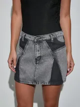 Minifalda de denim en color gris oscuro con diseño de paneles en contraste de lavado, tiro medio y cierre frontal con botón y cremallera.