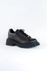 Zapatos de cuero negro con cordones, diseño robusto y suela track dentada. Presentan un detalle metálico en el centro de los cordones.