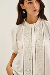 Camisa de algodón color celeste con cuello alto con volados, mangas tres cuartos abullonadas y cierre frontal con botones. Presenta un diseño con dos franjas verticales de bordado intrincado en color negro en el frente.