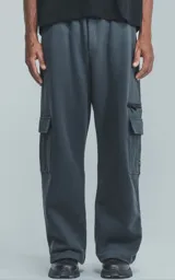 Pantalón tipo jogger de calce baggy, confeccionado en frisa pesada de algodón. Presenta una silueta amplia y relajada, cintura elástica, bolsillos laterales de mano y bolsillos cargo con solapa y cierre en los laterales.