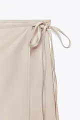 Falda corta tipo pareo, color marrón oscuro, confeccionada en tejido satinado con lazada ajustable en el lateral.