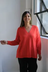 Sweater de punto color naranja, con cuello en V, manga larga y diseño holgado con tajos laterales en el ruedo.
