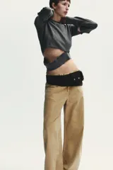 Jersey de punto gris oscuro, cuello redondo y manga larga. Presenta detalles desmontables con botones a lo largo de las costuras de las mangas y en el ruedo inferior.