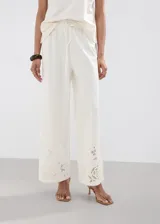Pantalón palazzo color blanco con detalles bordados en el bajo de las piernas, tiro medio y cintura elástica con cordón ajustable.