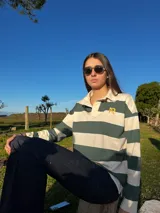 Sweater estilo rugby de manga larga con diseño de rayas horizontales anchas en color oliva y crudo. Presenta cuello tipo polo con cartera de botones y un logo bordado en color amarillo en el pecho.