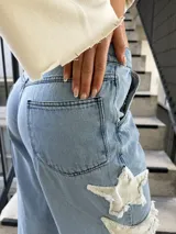 Jeans celestes de corte wide leg, tiro mid-rise, con grandes apliques de estrellas deshilachadas en tono crudo a lo largo del lateral de la pierna.