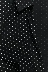 Camisa entallada de popelín negro con estampado de lunares blancos, escote en pico, cuello solapa y mangas muy cortas. Cuenta con costuras marcadas y cierre lateral con cremallera oculta.