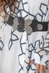 Cinturón ancho elástico y trenzado, con hebilla ornamental compuesta por círculos de fibra entrelazada en tonos gris y negro.
