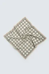 Pañuelo cuadrado de algodón color beige con estampado geométrico en negro y borde con líneas finas en rojo y verde oscuro.