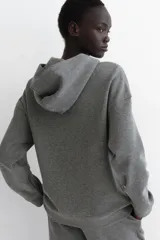 Campera de felpa gris melange con cierre frontal, capucha y bolsillos delanteros tipo canguro, de corte holgado y hombros caídos.