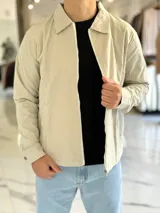 Campera de gabardina beige de corte boxy fit, con cuello camisero, cierre frontal de cremallera blanca y bolsillos laterales ribeteados.
