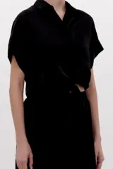 Camisa crop negra de tejido fluido y acabado brillante, con cuello camisero, mangas cortas con vuelta y nudo frontal en el dobladillo.