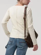 Remera de manga larga en color blanco hueso, con cuello redondo y cierre frontal parcial con botones. Presenta un diseño de tejido trenzado con textura en las mangas y cuerpo liso.