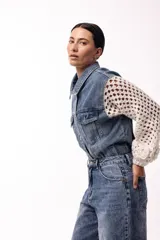 Campera de jean negra con mangas largas tejidas en crochet con diseño calado y detalles florales en relieve. Presenta cuello camisero, cierre frontal y bolsillos en el pecho.